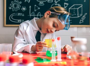 Boy dressed as chemist playing with chemistry game in front of a blackboard with drawings